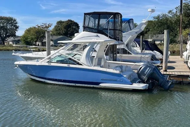 Slide: The Image of 2023 Chaparral 280 OSX boat docked in a marina, featuring a sleek blue and white design. - 25