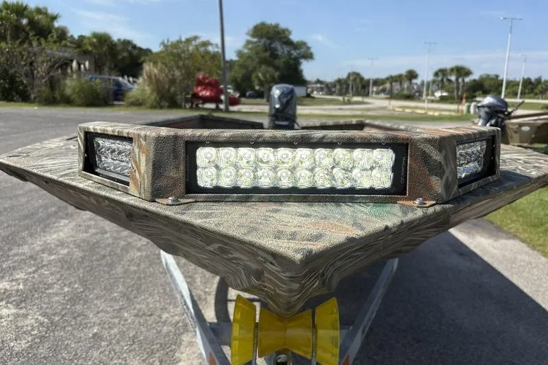 Slide: The Image of 2026 SeaArk 1752 Slayer boat with LED lights, camo design, parked outdoors. - 19