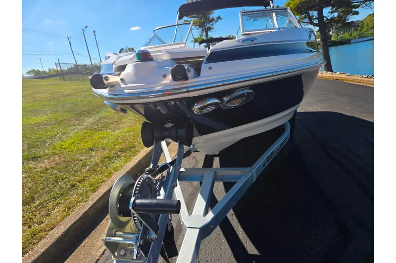 Slide: The Image of 2007 Larson LXi 228 boat on trailer, parked near a lake under clear blue sky. - 6