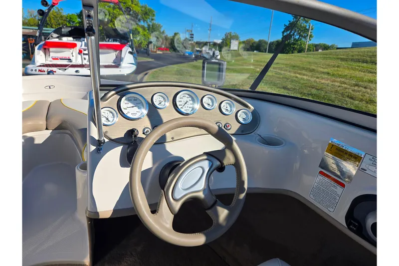 Slide: The Image of 2006 Tahoe Q4 Sport boat dashboard with steering wheel and gauges, parked outdoors. - 13