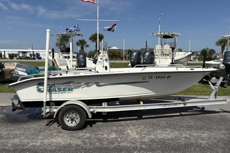 Slide: The Image of 2004 Carolina Skiff 175 boat on trailer, parked outdoors with flags in the background. - 2