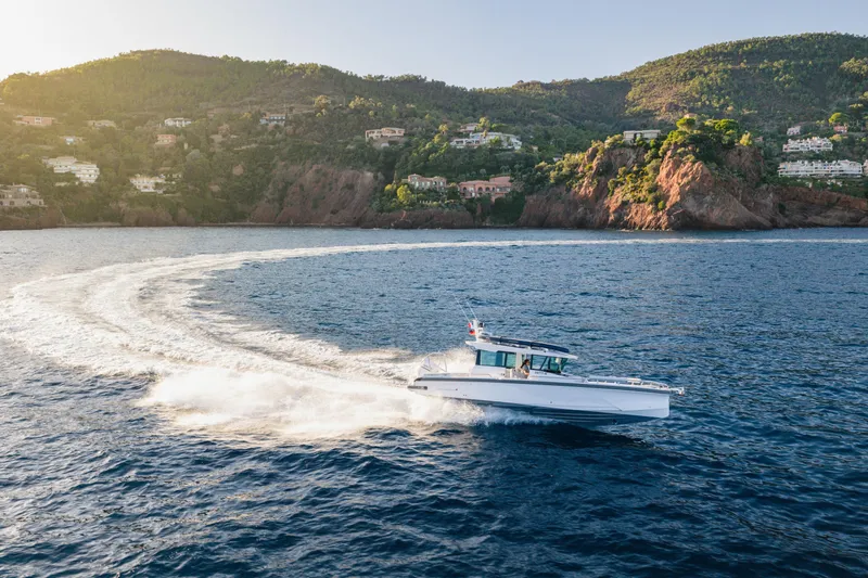 Slide: The Image of 2026 Axopar 29 XC cruising on scenic coastal waters with lush hills in the background. - 3