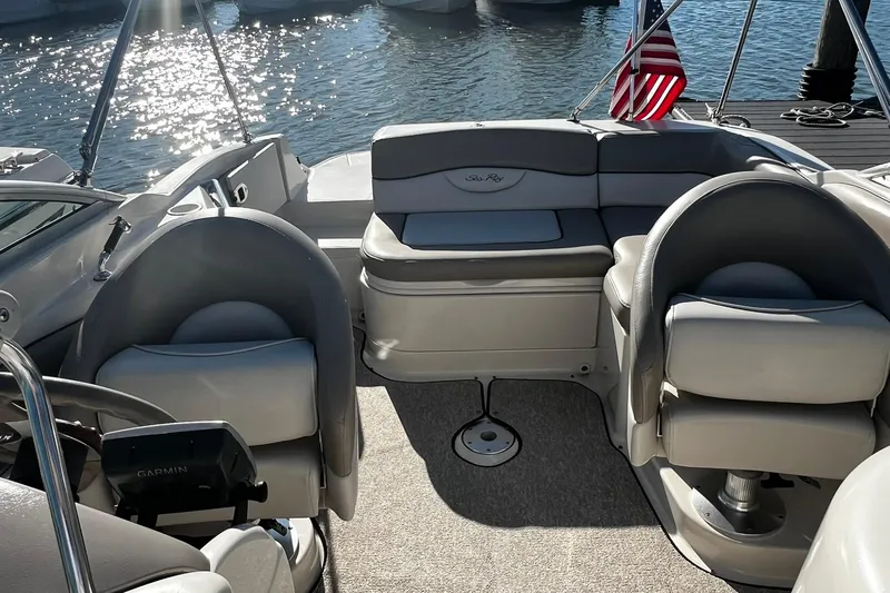 Slide: The Image of 2003 Sea Ray 220 Sundeck interior with seating, steering, and American flag by the water. - 8