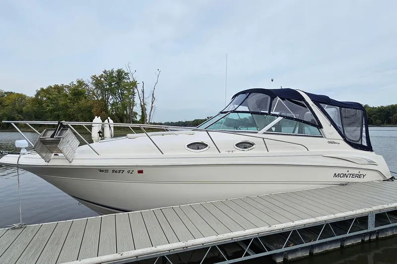 The Image of 2004 Monterey 282 Cruiser docked on a calm lake with trees in the background. - 1