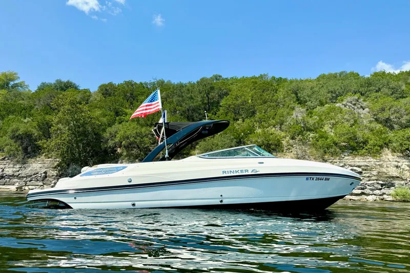 Slide: The Image of 2011 Rinker 276 Captiva boat on water with American flag, lush greenery background. - 2