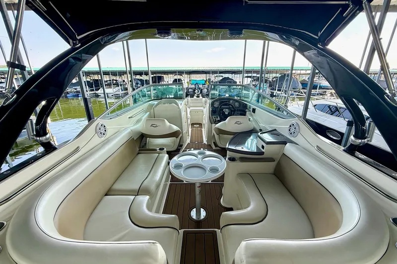 Slide: The Image of 2011 Rinker 276 Captiva boat interior with beige seating and wood accents at a marina. - 21