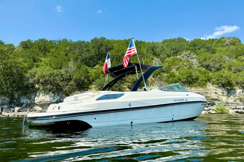 Slide: The Image of 2011 Rinker 276 Captiva boat on water, flags waving, lush green shoreline background. - 3