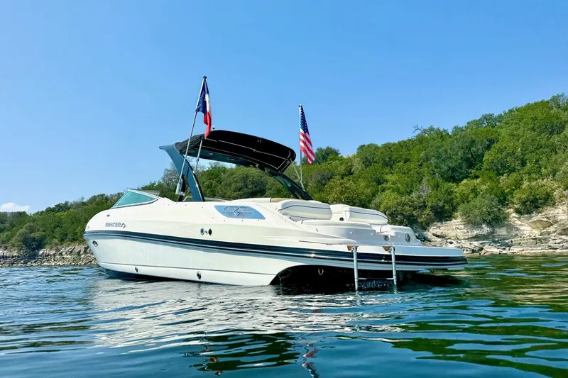 Slide: The Image of 2011 Rinker 276 Captiva boat on water, flags flying, scenic green shoreline. - 6