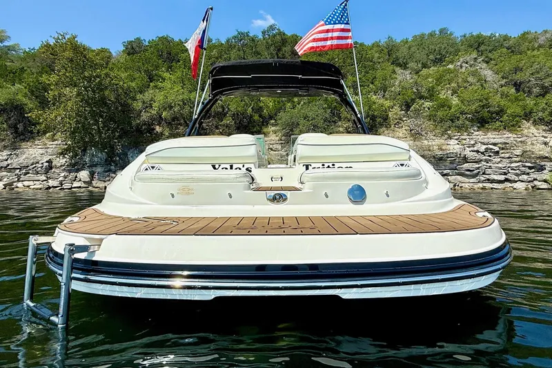 Slide: The Image of 2011 Rinker 276 Captiva boat on water with flags, near rocky shoreline. - 8