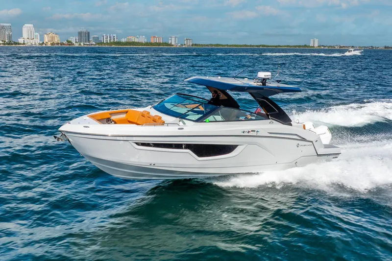 Slide: The Image of 2024 Cruisers Yachts 34 GLS OB cruising on open water, city skyline in background. - 2