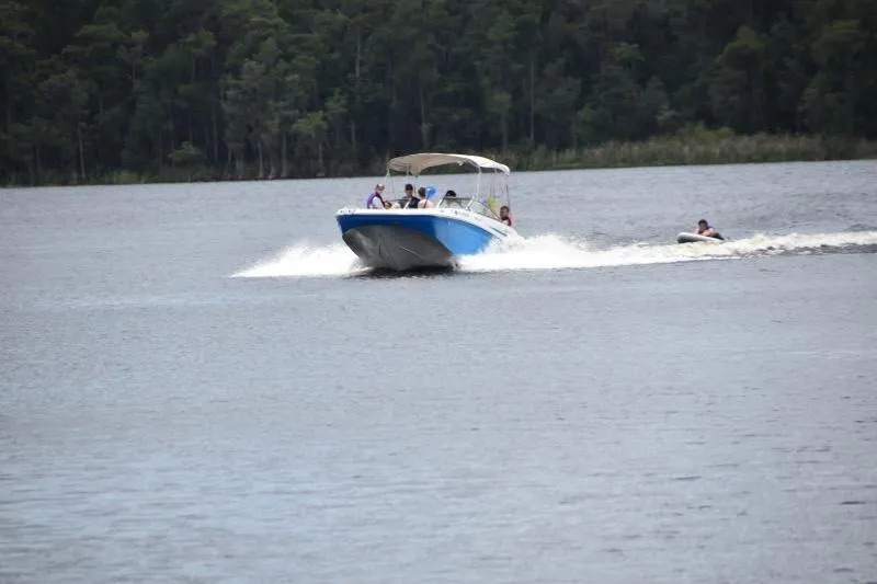 Slide: The Image of 2020 Hurricane SunDeck 191 OB boat cruising on a lake with people tubing behind. - 6