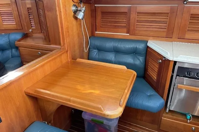 Slide: The Image of Gozzard 37 yacht interior with wooden table, blue seating, and compact kitchen area. - 19