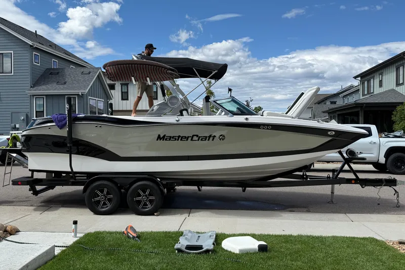 Slide: The Image of 2021 MasterCraft X24 boat on trailer, parked in residential area under blue sky. - 0