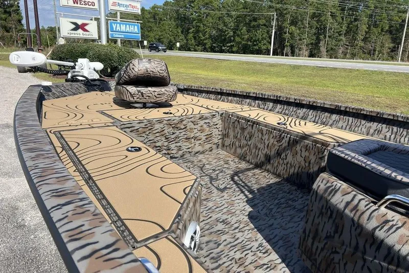 Slide: The Image of 2026 Xpress H22B Bay boat with camouflage design, parked near dealership signs. - 7