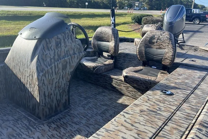 Slide: The Image of 2026 Xpress XP170 boat interior with camouflage seats and console, parked outdoors. - 12