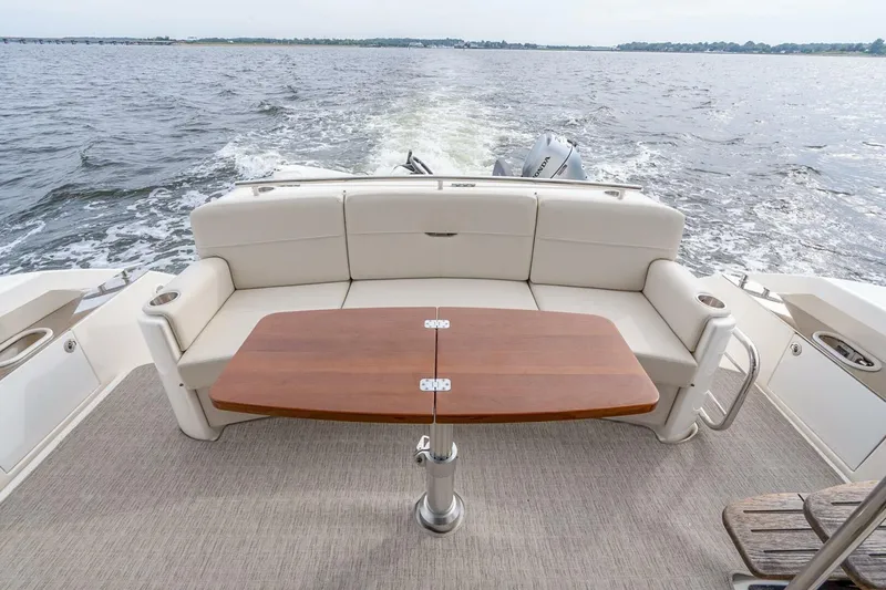 Slide: The Image of 2021 Tiara Yachts F44 Flybridge aft deck with seating and wooden table on open water. - 11