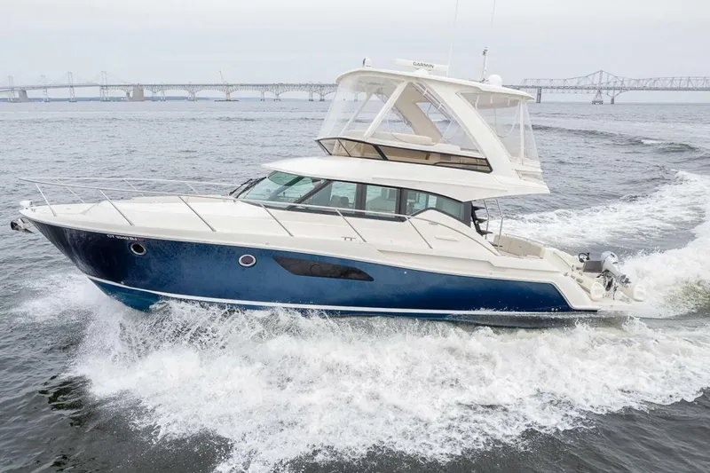 Slide: The Image of 2021 Tiara Yachts F44 Flybridge cruising on open water near a bridge. - 6