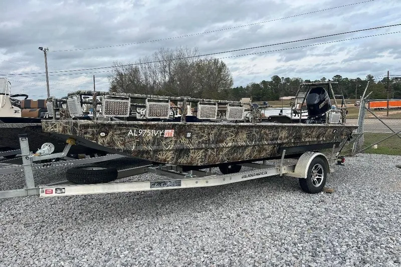 The Image of Camouflage-patterned 2024 Custom 1854 boat on trailer, parked on gravel lot. - 0