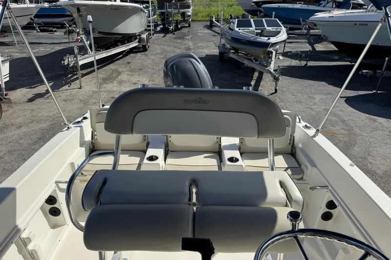 Slide: The Image of 2015 NauticStar 231 Angler boat interior with seating and steering wheel, parked among other boats. - 15