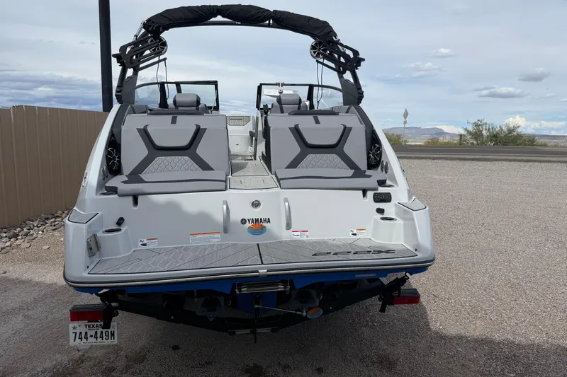 Slide: The Image of 2024 Yamaha Boats 222XD, rear view, parked on gravel, showcasing seating and design. - 6