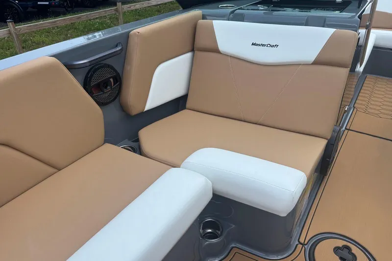 Slide: The Image of 2025 MasterCraft NXT24 boat interior with tan and white seating, featuring cup holders and speaker. - 10