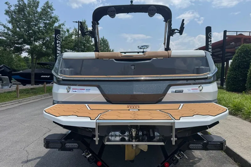Slide: The Image of 2025 MasterCraft NXT24 boat rear view with teak swim platform, parked outdoors. - 6