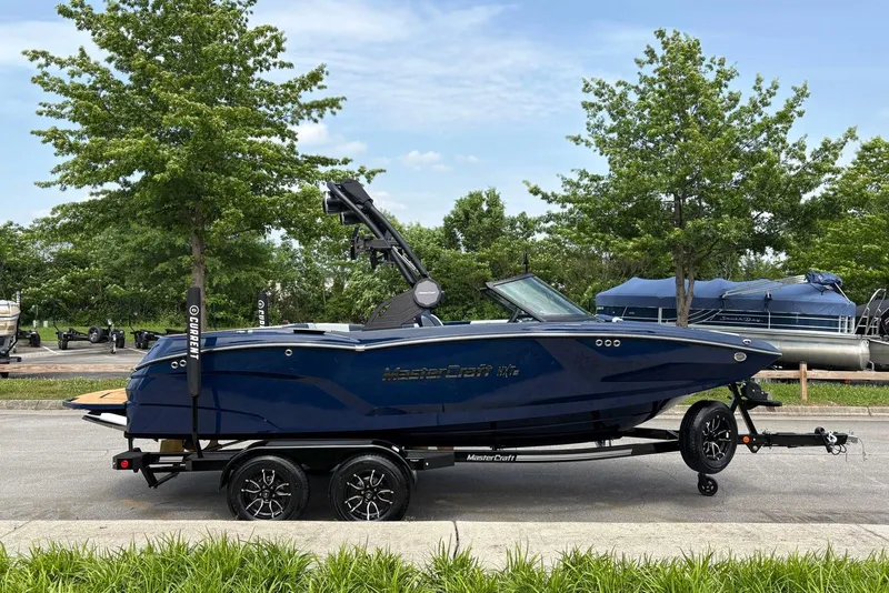 The Image of 2025 MasterCraft NXT20 boat on trailer, parked outdoors with trees in background. - 0