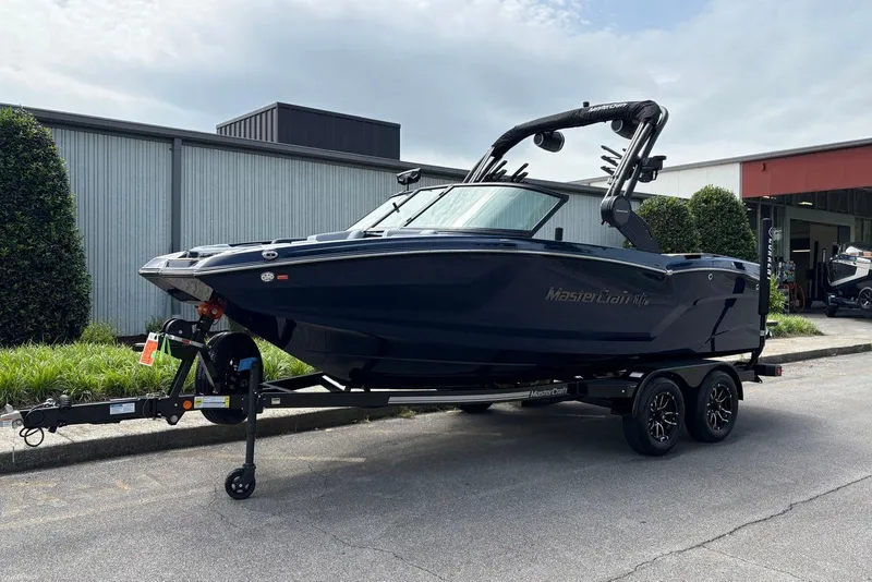 Slide: The Image of 2025 MasterCraft NXT20 boat on trailer, parked outdoors near a building. - 2