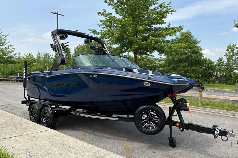 Slide: The Image of 2025 MasterCraft NXT20 boat on trailer, parked outdoors, surrounded by trees. - 3