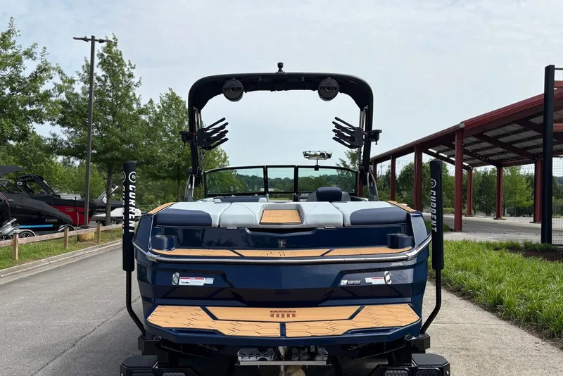 Slide: The Image of 2025 MasterCraft NXT20 boat, rear view, parked outdoors with trees and a building nearby. - 6