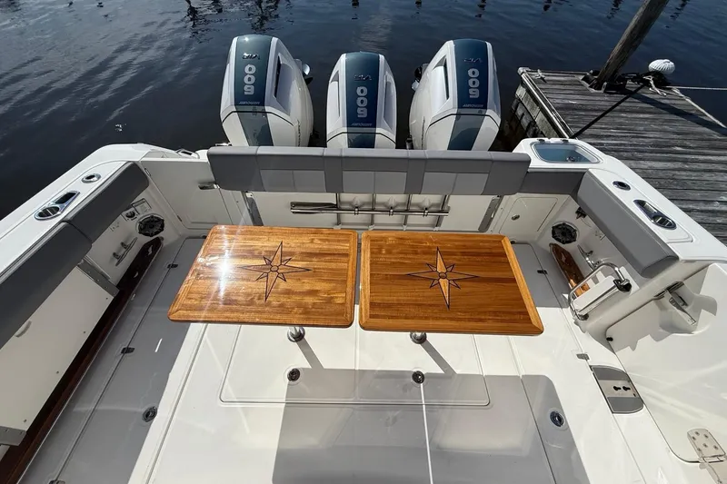 Slide: The Image of 2024 Boston Whaler 420 Outrage boat deck with wooden tables and triple outboard engines. - 16