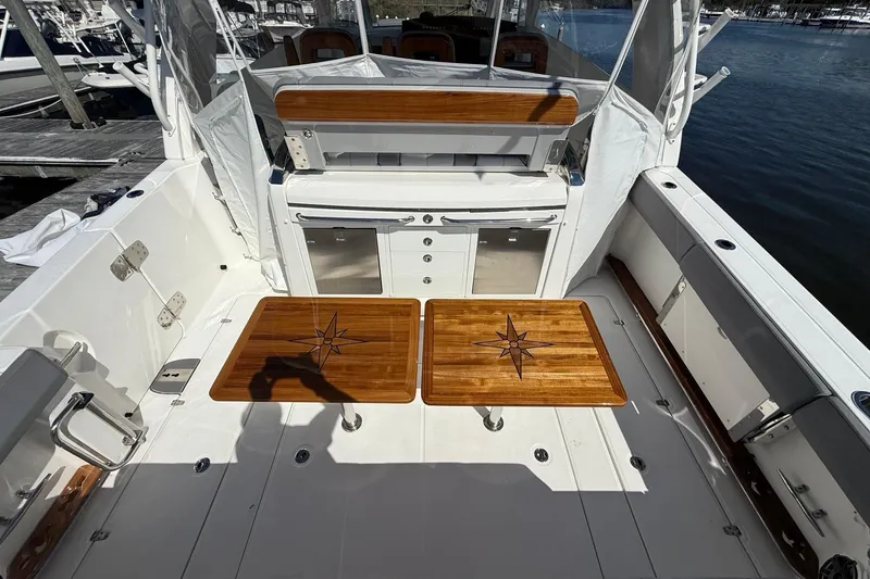 Slide: The Image of 2024 Boston Whaler 420 Outrage cockpit with wooden tables and seating, docked by the water. - 17
