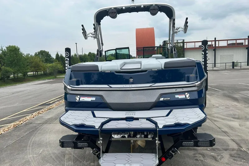 Slide: The Image of 2025 MasterCraft NXT23 boat, rear view, parked outdoors, showcasing sleek design and swim platform. - 2