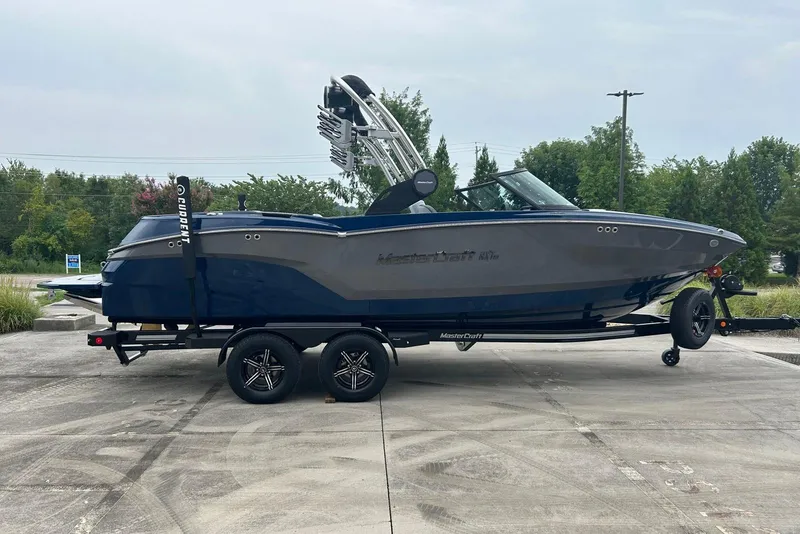 Slide: The Image of 2025 MasterCraft NXT23 boat on trailer, parked outdoors, side view. - 5
