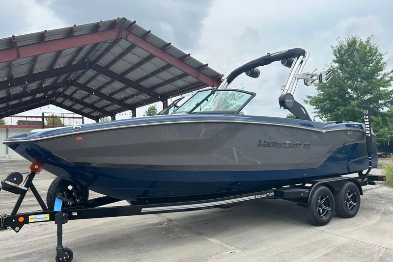 Slide: The Image of 2025 MasterCraft NXT23 boat on trailer under metal canopy, side view. - 6