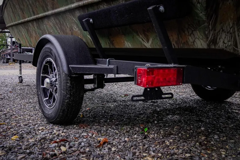 Slide: The Image of Trailer of 2026 G3 17SC boat on gravel, featuring camo design and red reflector. - 15