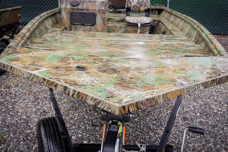 Slide: The Image of Camouflage-patterned 2026 G3 17SC boat on gravel, featuring a spacious deck and seating. - 3
