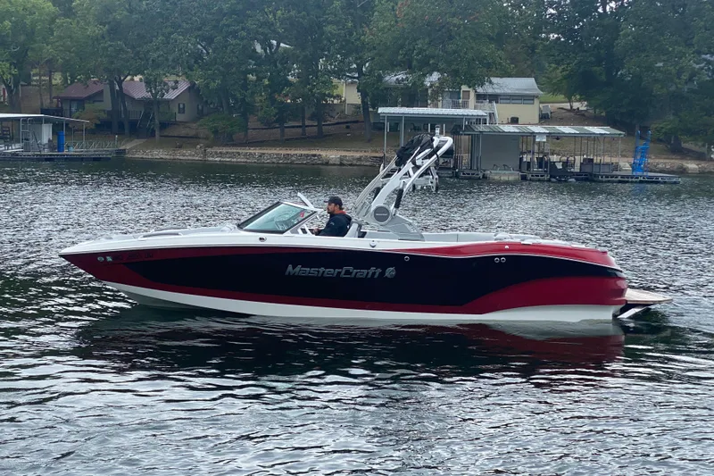 Slide: The Image of 2019 MasterCraft X24 boat cruising on a lake near a wooded shoreline. - 4