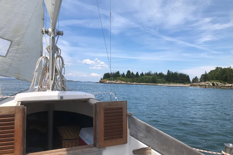 Slide: The Image of Sailing on a 1970 Bluenose One Design boat near a scenic, tree-lined shoreline. - 2