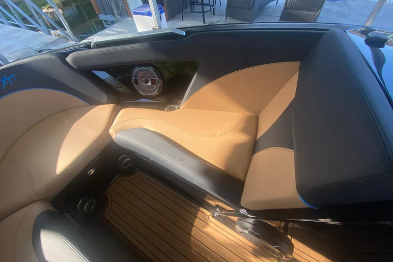 Slide: The Image of 2021 MasterCraft XT25 boat interior with tan and black seating, featuring a speaker and wood flooring. - 28