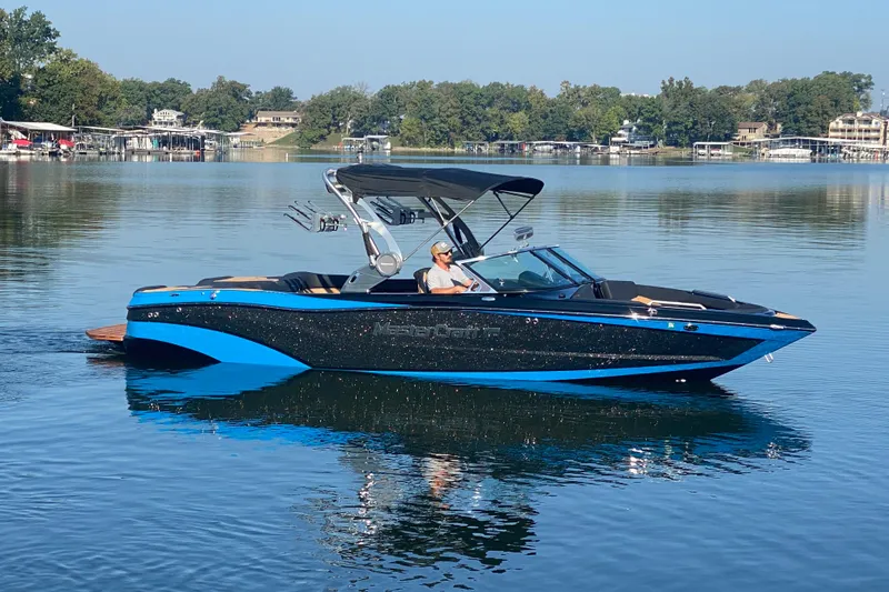 Slide: The Image of 2021 MasterCraft XT25 boat on a calm lake, featuring sleek black and blue design. - 6