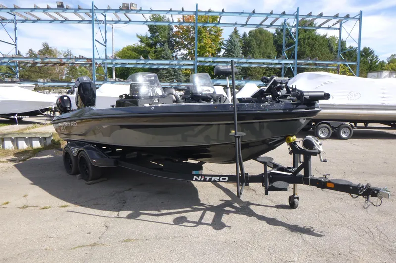 Slide: The Image of 2023 Nitro ZV21 boat on trailer, parked outdoors, surrounded by trees and other boats. - 21