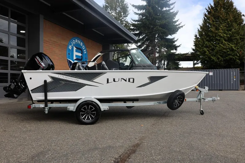 Slide: The Image of 2026 Lund 1775 Adventure Sport boat on trailer, parked outdoors near building. - 2