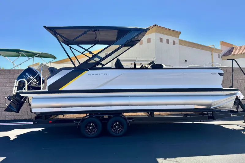 The Image of 2025 Manitou EXPLORE 24 pontoon boat on trailer, featuring sleek design and Suzuki outboard motor. - 0