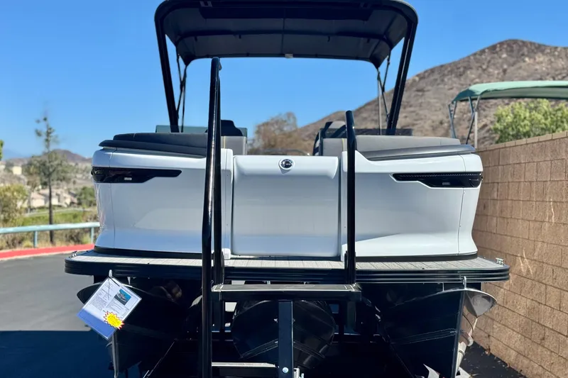 Slide: The Image of 2025 Manitou EXPLORE 24 pontoon boat, rear view, parked outdoors with scenic background. - 2