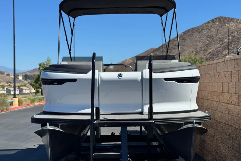 Slide: The Image of 2024 Manitou Cruise 22 pontoon boat, rear view, parked near mountains. - 2