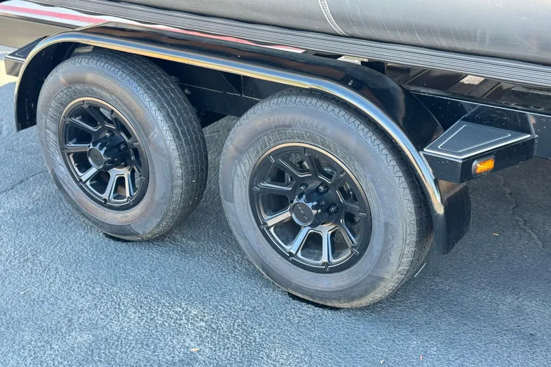 Slide: The Image of Trailer wheels of a 2024 Manitou Cruise 22, featuring black rims on asphalt. - 23