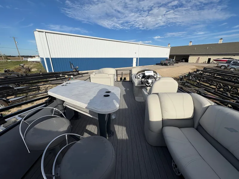 Slide: The Image of 2018 Starcraft CX 23 RE pontoon boat with spacious seating and table, parked outdoors. - 11