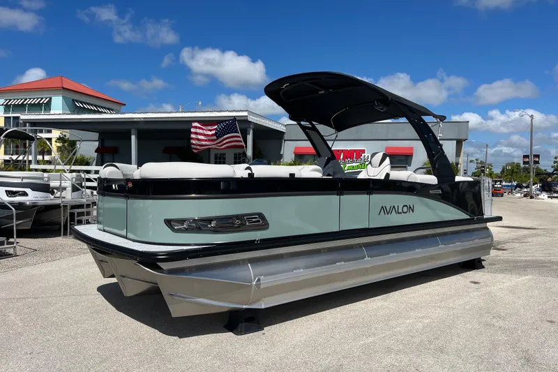 Slide: The Image of 2026 Avalon 2385 Catalina Quad Lounger Tri Toon boat with American flag, parked outdoors. - 1
