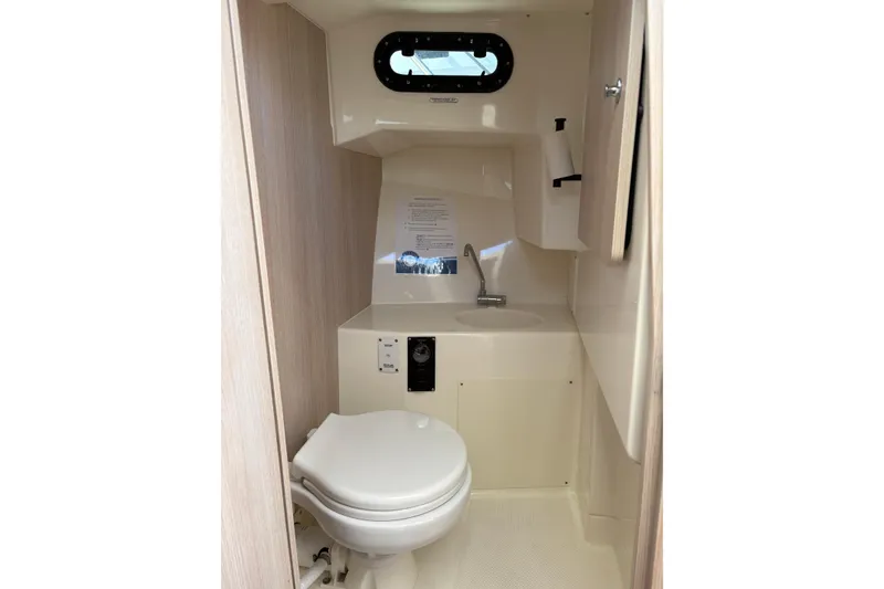 Slide: The Image of 2023 Bayliner Trophy T25 Pilothouse bathroom with toilet, sink, and porthole window. - 9